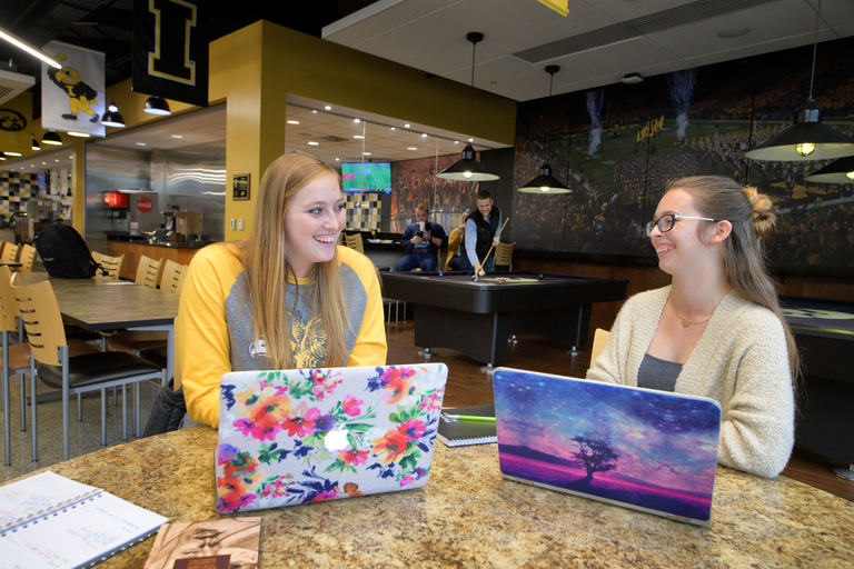 Two student with laptops talking with one another