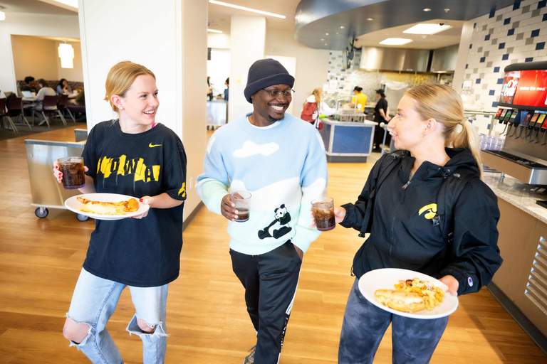 Two girls and one male talk with one another and carrying plates of food