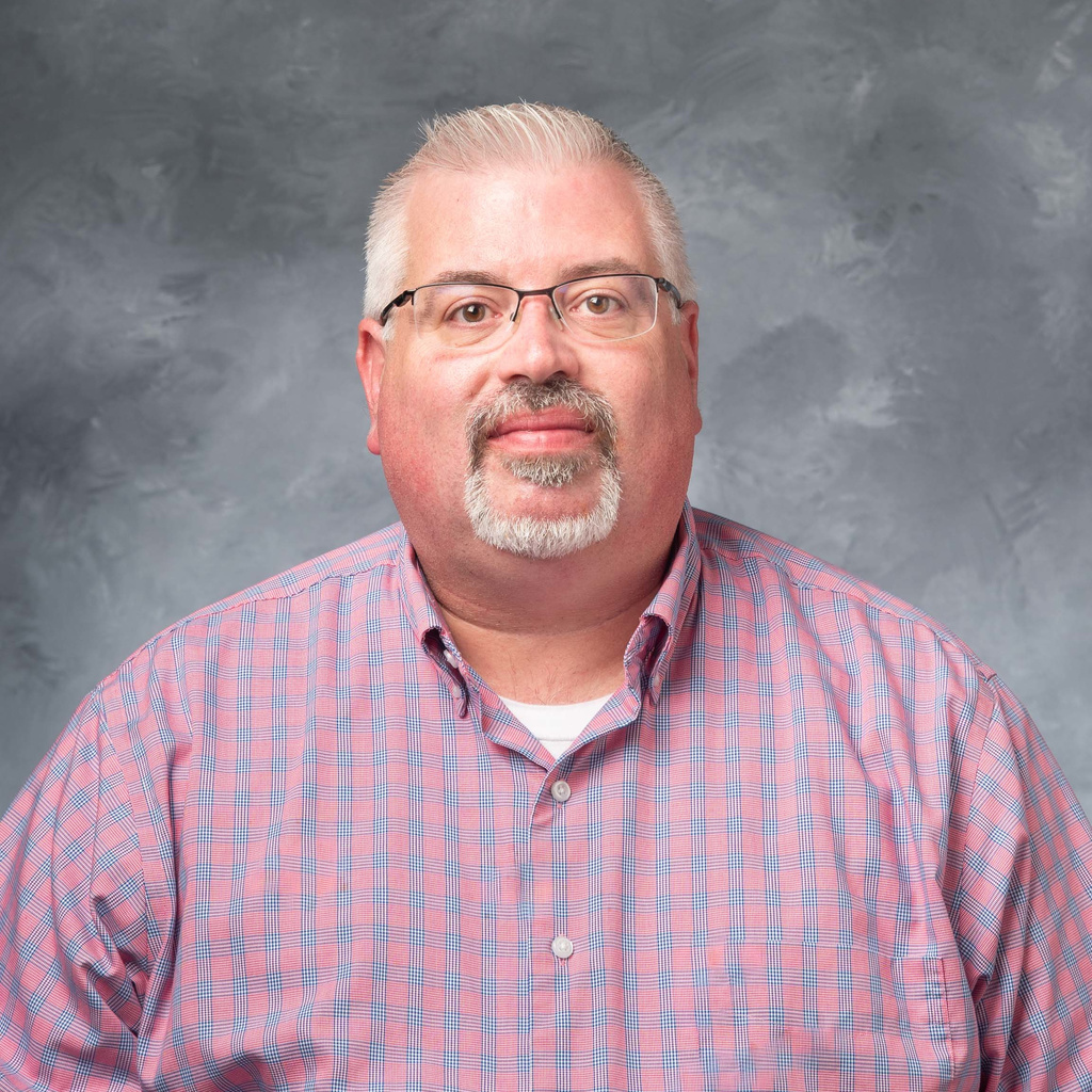 portrait of the director of dining, a man wearing glasses with gray hair and a goatee, wearing a pink plaid shirt.