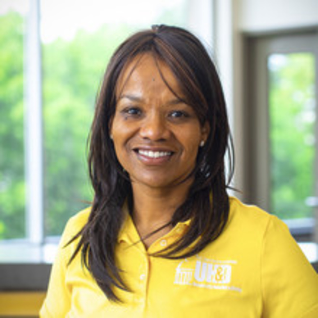 Portrait of Chef Crystal, shoulder-length dark hair with reddish highlights, smiling Black woman wearing yellow shirt