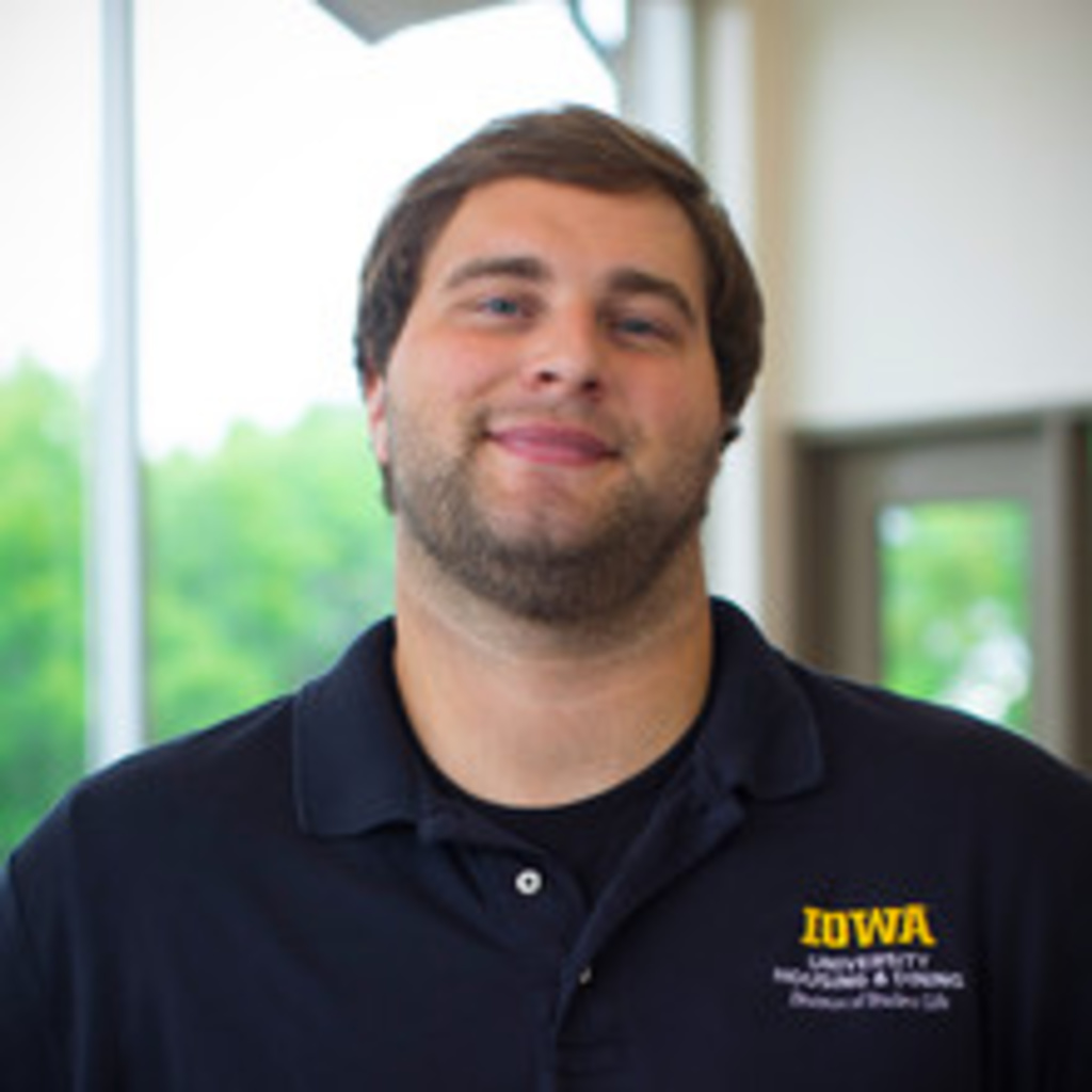 headshot of assistant manager Brandon Aggson, a white man with brown hair wearing black collared shirt
