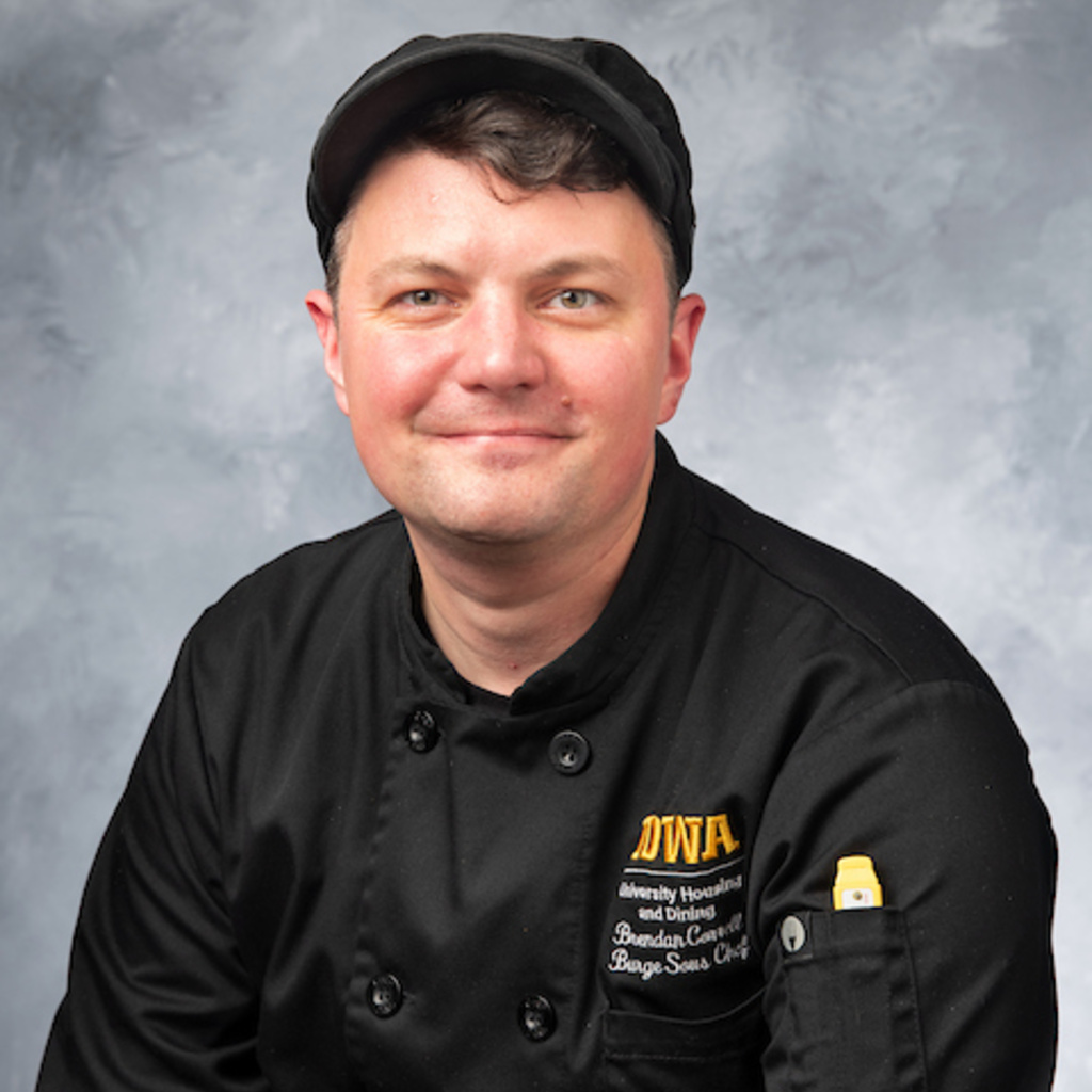 headshot of man wearing black chef's coat and cap