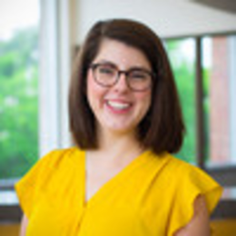 Portrait of school nutritionist in yellow shirt, wearing brown hair in a bob in front of a window where green trees are in the outside background