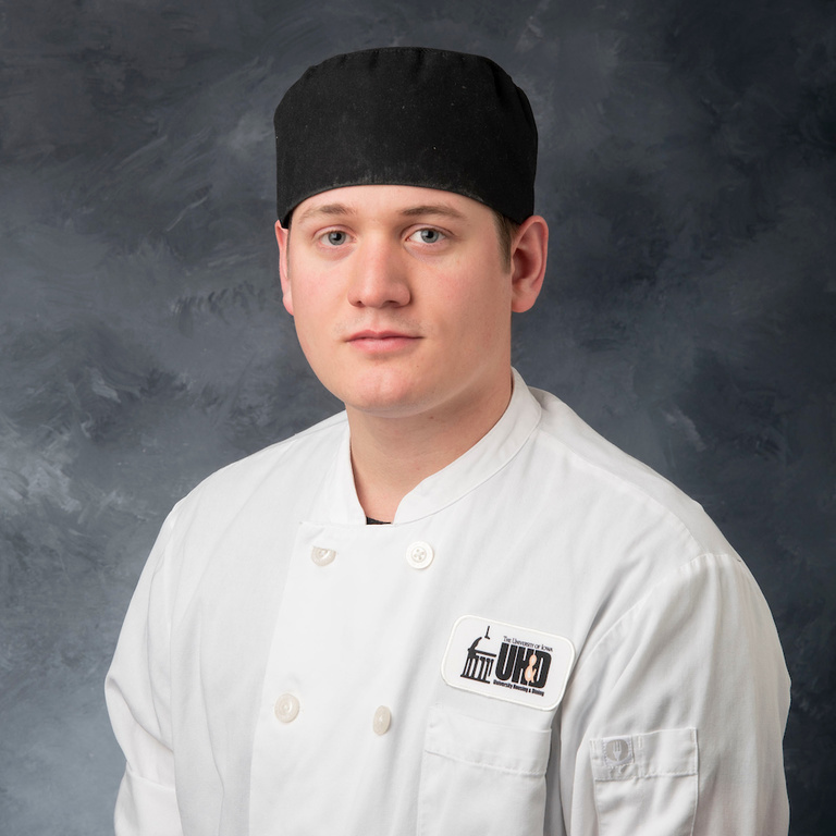 headshot of sous chef Pete Schuessler, white man wearing black cap and white chef's coat