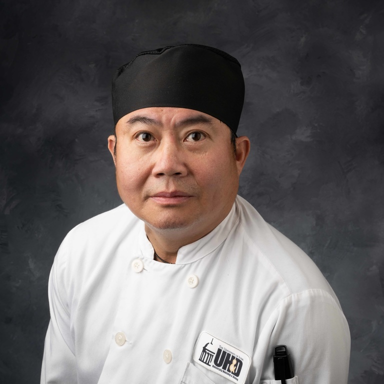 Headshot of sous chef Justyn Tran, Vietnamese man wearing white chef's coat