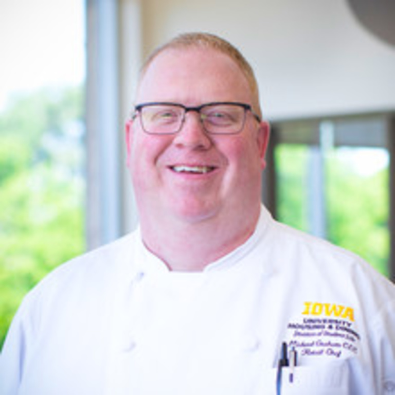 headshot of white man in chef's coat and horn rimmed glasses