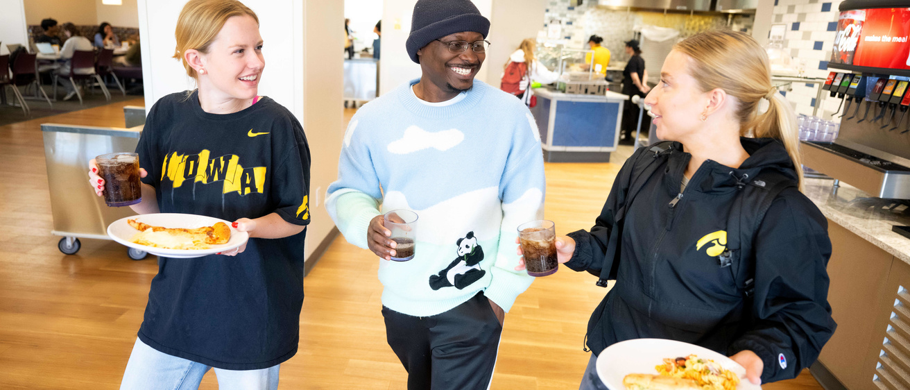 Two girls and one male talk with one another and carrying plates of food
