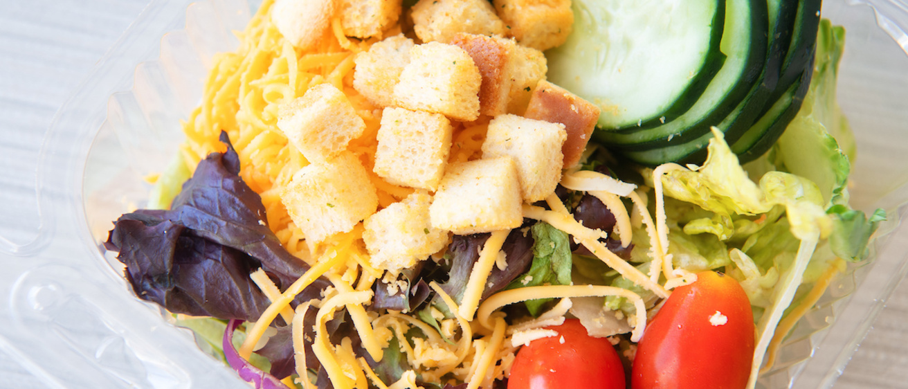 To-go salad option at retail locations, featuring tomatoes, cucumber slices, shredded cheese, croutons, lettuce